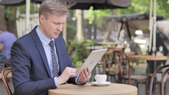 Businessman Upset By Loss on Tablet Sitting in Outdoor Cafe