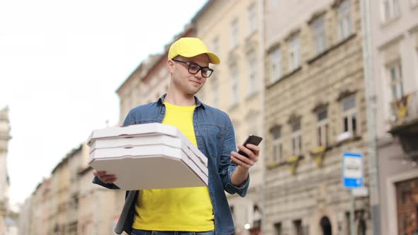 A Young Happy Delivery Man is Standing and Holding Three Pizza Boxes