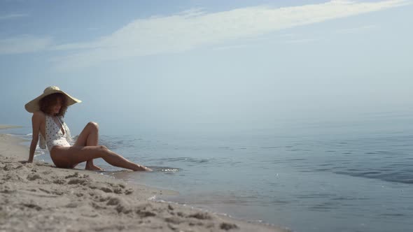 Relaxed Woman Sitting Beach Sand Washing Legs in Ocean Waves