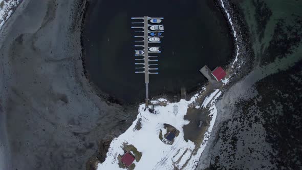 Aerial dolly shot of Ase harbor looking down onto boats the dock and breakwater with light snow and