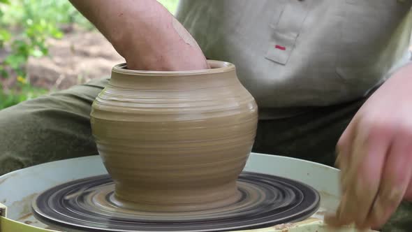 Male Makes a Clay Jug on a Rotating Circular Loom Outdoors on a Sunny Bright Day