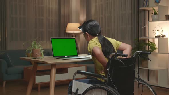 Kid Girl Sitting In A Wheelchair Using Laptop Computer With Mock Up Green Screen And Pain Her Back