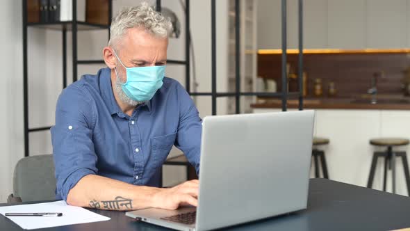 Mature Grayhaired Male Employee Wearing Medical Mask is Using Laptop at the Office