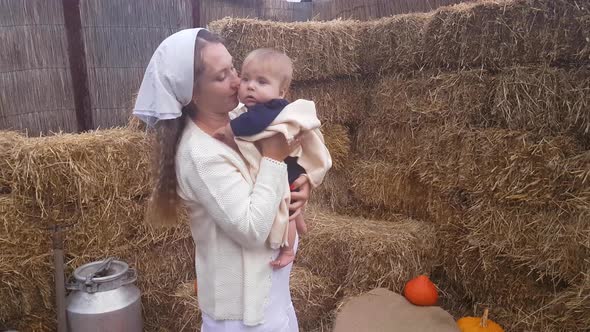 A young mother holds a baby boy with bare feet in her arms, gently kisses and hugs