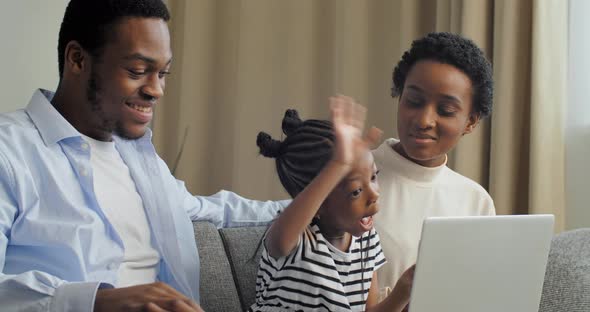 Side View of Parents with Little Daughter Looking at Laptop Listening To Lesson Communicating with