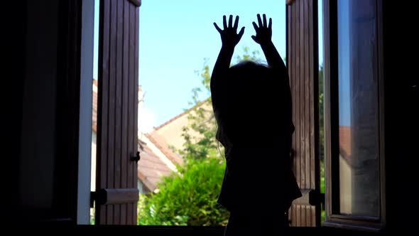 Silhouette of a Happy Girl Waving Her Hands on the Background of an Open Window