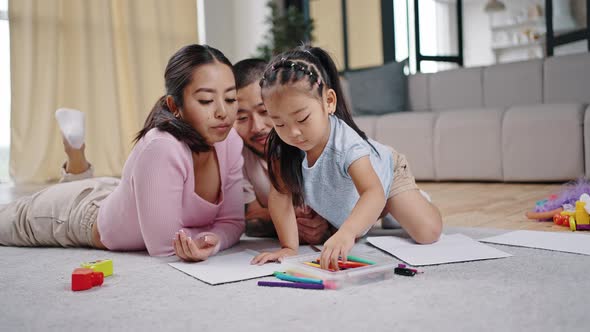 Asian Daughter Tries to Draw Picture with Happy Parents