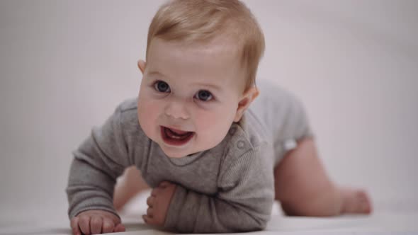 A 6-month-old baby is learning to crawl on a light background and smiling