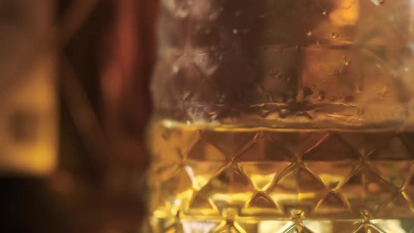Dolly in Footage Close Up View of Faceted Glass of Whiskey or Other Golden Alcoholic Beverage