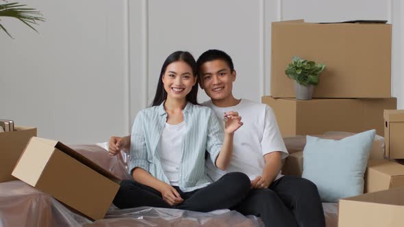 Japanese Couple Showing Key Sitting Among Boxes In New Home