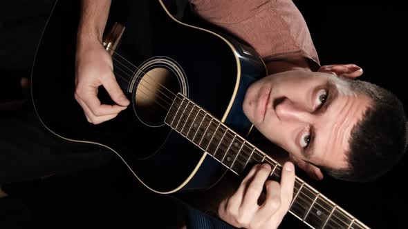 Vertical video. Young man plays an acoustic guitar on a black background