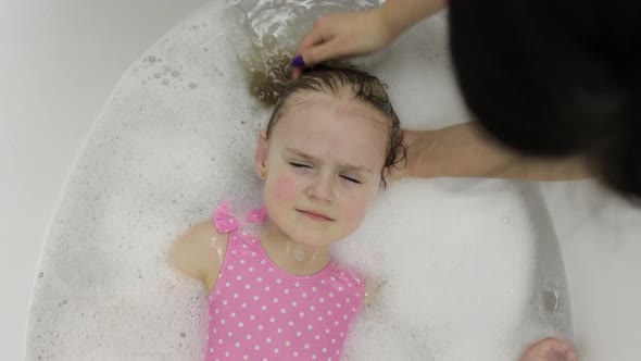 Cute Blonde Girl Takes a Bath in Swimwear. Little Child Washes Her Head