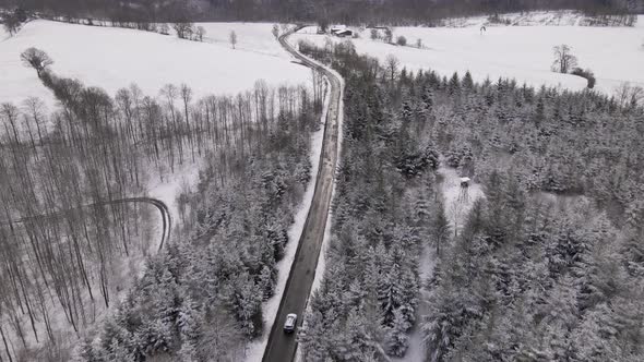 Two cars travelling along an open road through snow covered forest and fields in the picturesque cou