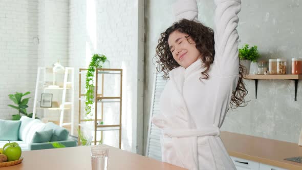 Happy Sleepy Woman Stretching and Drinks a Glass of Water in Early Morning