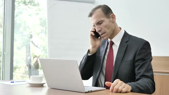 Businessman Talking on Phone and Using Laptop