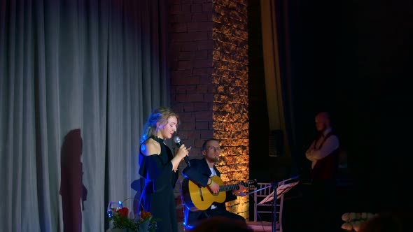 A Man Plays the Guitar on the Stage of the Auditorium and a Young Singer Sings