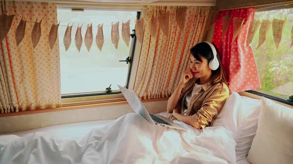 Young woman traveler laying in camper van and using laptop while road trip traveling on vacation