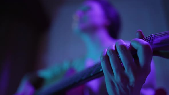 Musician Plays Guitar on Stage Illuminated By Purple Light