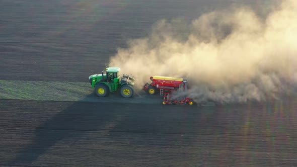 Green tractor cultivating ground and seeding a dry field. Aerial view of the tractor in the field.