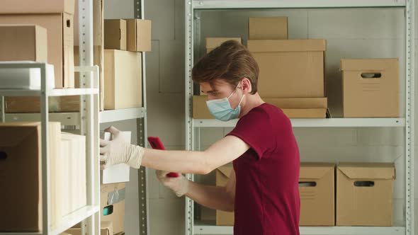 Man Employee of Warehouse Wearing Medical Mask and Gloves Taking Photo of Parcels on Smartphone