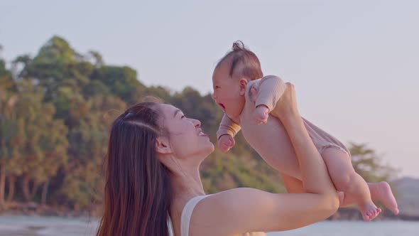 Happy Asian mom raise baby up playing and laughing together with sunset light