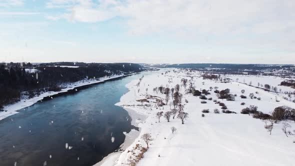 Flowing winter river and landscape during snowfall, aerial drone view