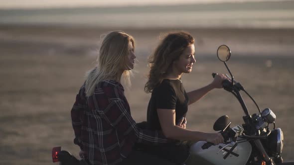 Attractive Young Woman Motorcyclist with His Girlfriend Riding a Motorcycle in a Desert on Sunset or