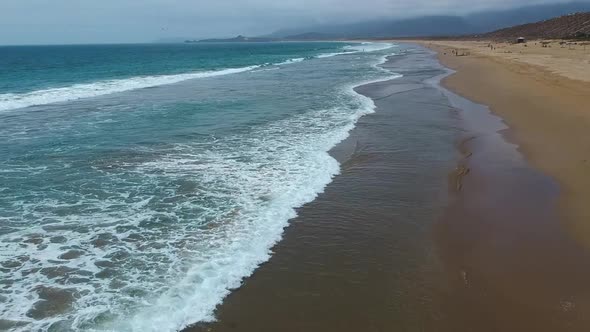 one side the ocean the other the sandAerial shot moving forwards along the waves