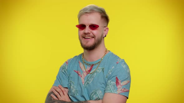 Seductive Cheerful Stylish Man in Blue Tshirt Wearing Sunglasses Charming Smile on Yellow Wall