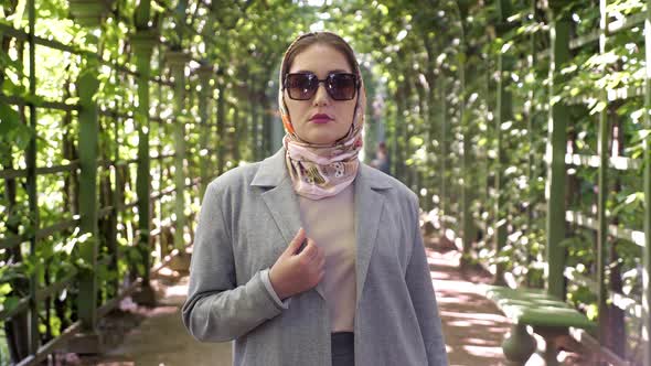 Woman in Headscarf and Sunglasses Smiling in Garden Arch