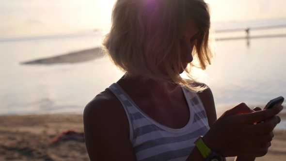 Woman Using Smart Phone At Sunset By The Sea