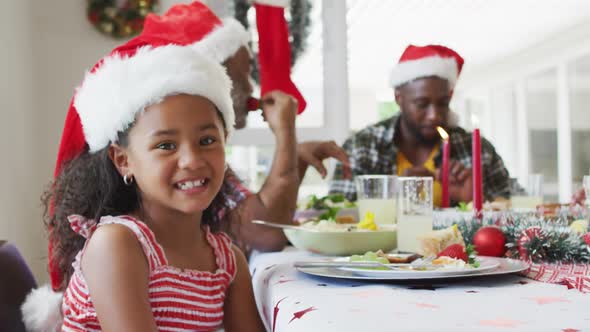 Portrait of smiling african american girl wearing santa hat celebrating holiday meal with family