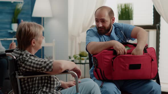 Old Woman in Wheelchair Receiving Bottle of Pils From Man Nurse