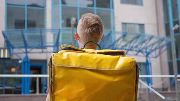 Back View Young Man with Yellow Thermal Food Delivery Backpack Looking at Business Center Turning