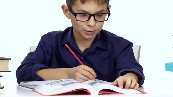 Boy Sits at a Table Recording Something Into Her Notebook and Flips Through the Book. White