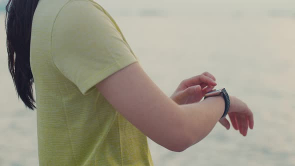 Beautiful woman runner standing outdoors checking fitness progress on her smartwatch.