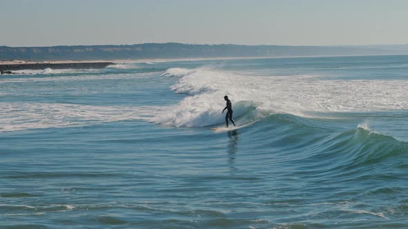 Surfer standing on a blue wave while surfing at the Atlantic Ocean 