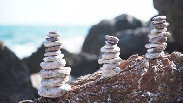 Three Balanced Pyramids of Stones on the Beach on the Background of Sea Waves