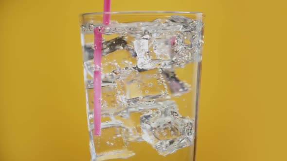 Somebody Mix Water Drink with Drinking Straw. Glass Full of Fizzy with Ice Cubes Yellow Background