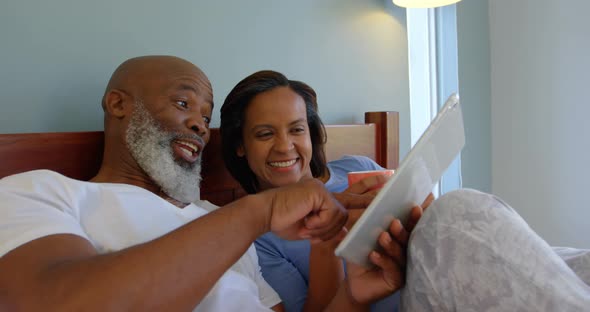 Front view of mature Caucasian couple using digital tablet on bed in a comfortable home 4k