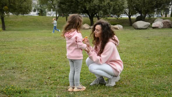 Happy Mom and Little Daughter Play on the Lawn