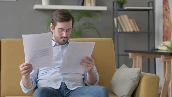 Young Man Reacting to Loss on Documents Sofa