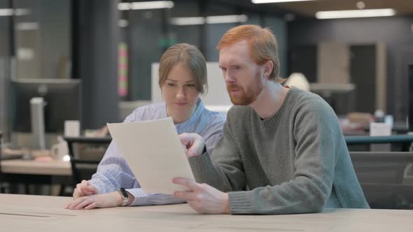 Young Man and Woman Reading Documents in Office