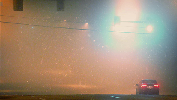 Car Driving Past Traffic Lights In Snowfall alt