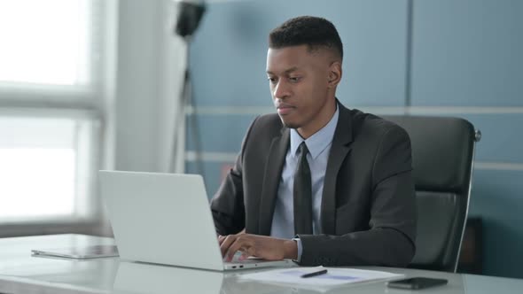 African Businessman Looking at Camera while using Laptop in Office