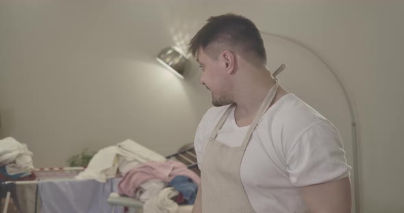 Exhausted Caucasian Man Looking Back at Pile of Laundry on Dryer and Rubbing Head with Hands