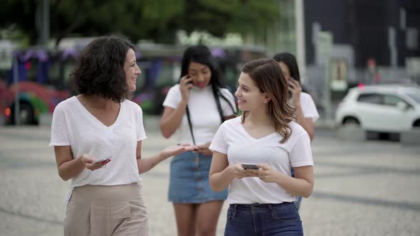 Smiling Women Talking and Holding Phones During Stroll