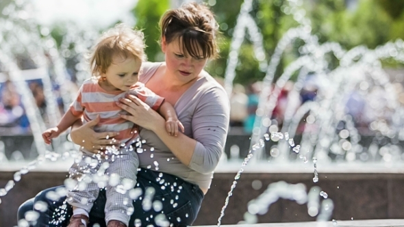 Mother And Baby Boy Playing With Fountains