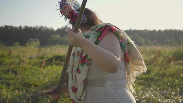 Cute Plump Woman with a Wreath on Her Head Mowing the Grass with the Scythe on the Green Summer