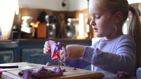 Close up footage of a young five year old girl playing with clay in the kitchen of the house she liv